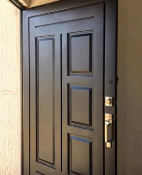 Puerta de metal negra con paneles en relieve y cerradura dorada